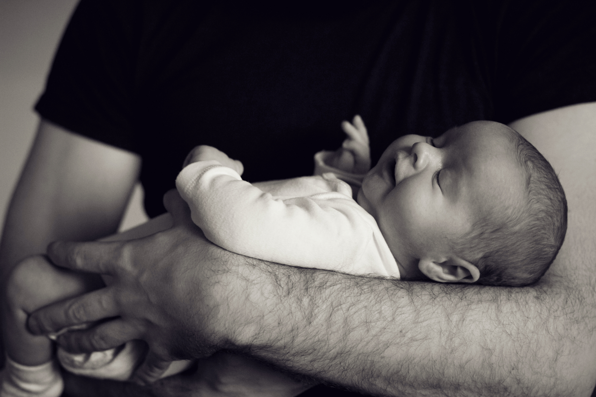 Bild: Ein glückliches Baby liegt geborgen in den Armen seines Vaters